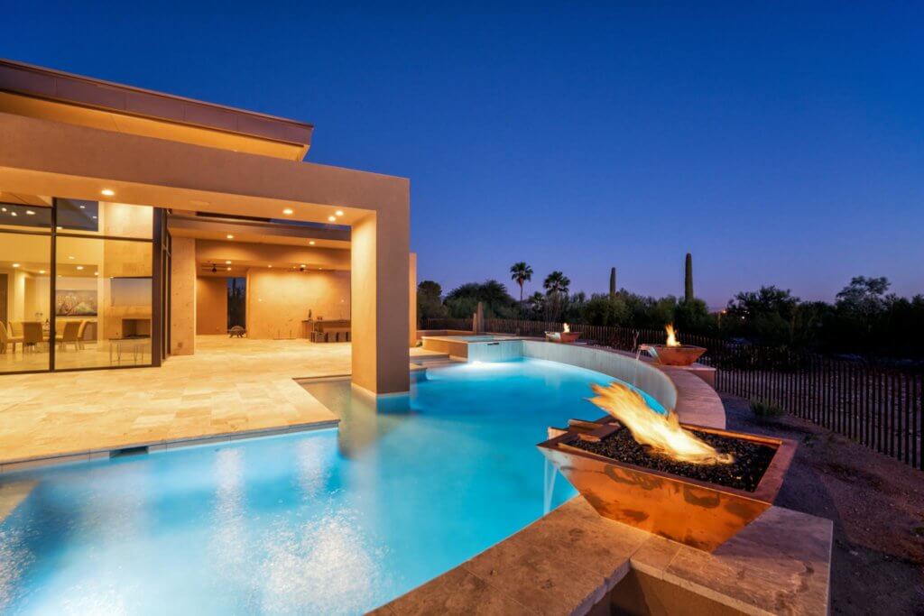 A modern home with a large curved pool illuminated at night
