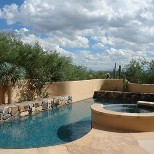 Custom landscape design surrounding a pool with a hot tub
