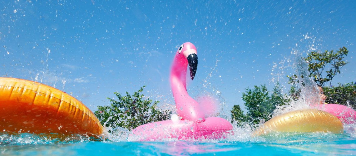 Funny action photo in the outdoor swimming pool with splashes of inflatable flamingo and doughnuts buoys rings